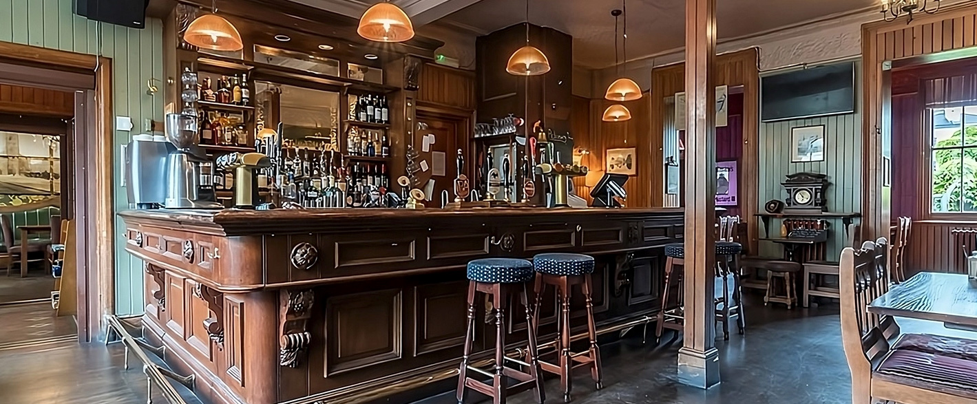 The interior of The Warwick Castle, featuring wooden floors and a beautiful carved wooden bar